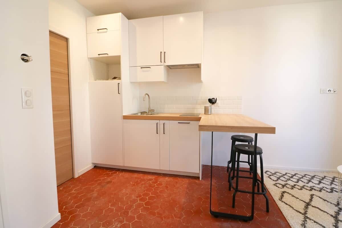 Uma cozinha compacta com armários brancos, bancada de madeira e um banquinho.