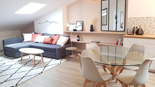 Een moderne woonkamer met een hoekbank, een glazen eettafel en een kleine ronde tafel.