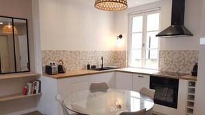 Een moderne keuken met een ronde glazen tafel, witte kasten en een inbouwoven.