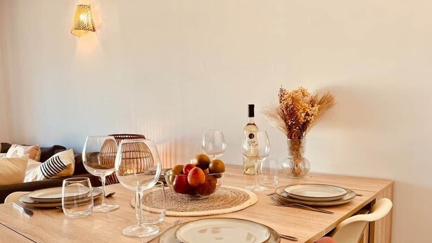 Ein Holztisch ist gedeckt mit Tellern, Gläsern, Besteck, einer Obstschale und einer Flasche.