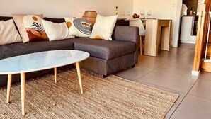 Ein modernes Wohnzimmer mit einem Ecksofa, einem runden Couchtisch und einem durch einen Bogen sichtbaren Küchenbereich.