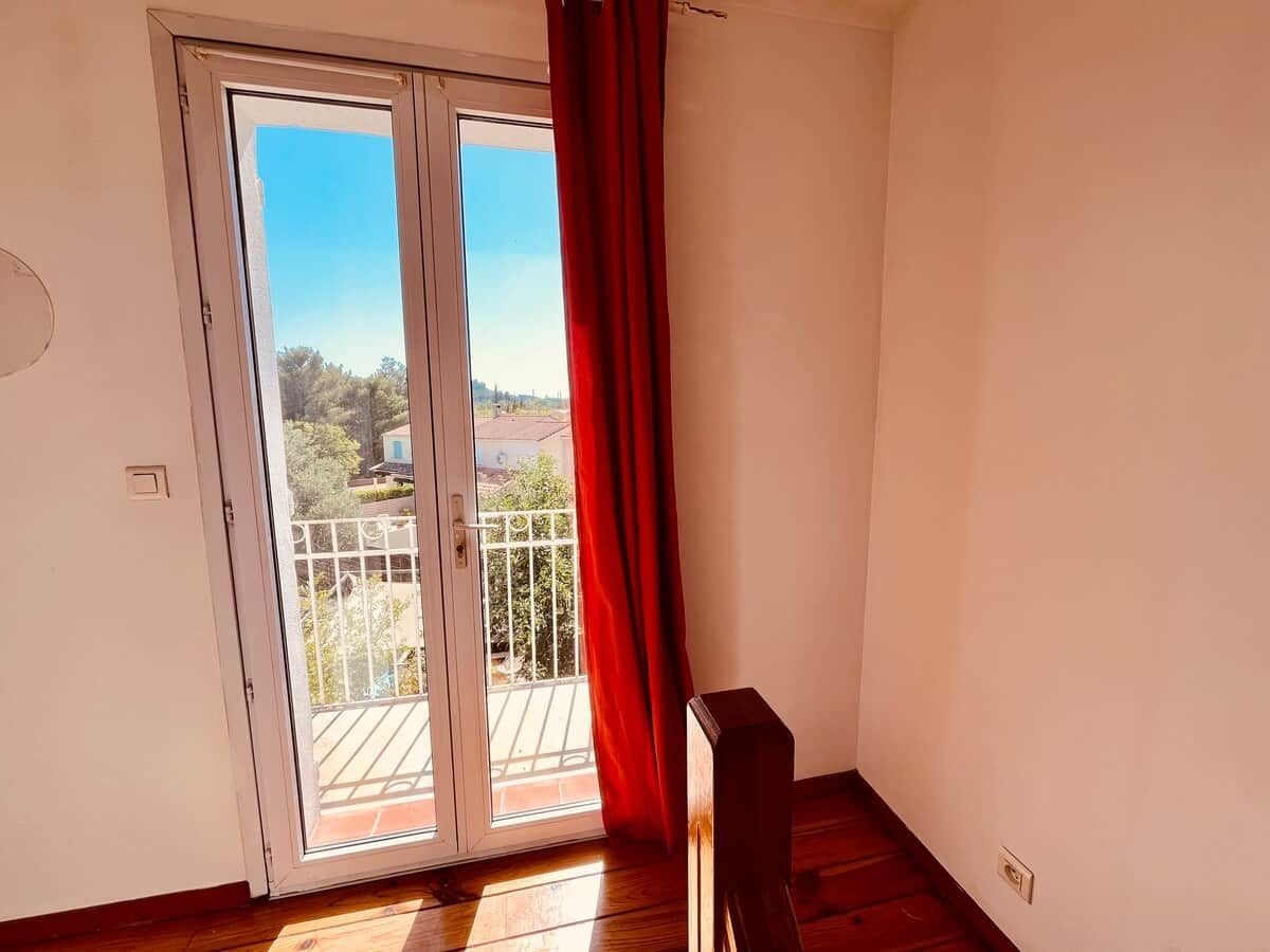Una habitación con puerta corrediza de vidrio que da a un balcón exterior, suelo de madera y cortina roja.