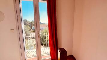 Una habitación con puerta corrediza de vidrio que da a un balcón exterior, suelo de madera y cortina roja.