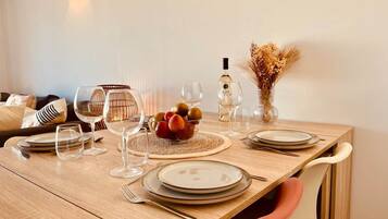 Una mesa de madera dispuesta con platos, vasos, cubiertos, un cuenco de fruta y una botella.