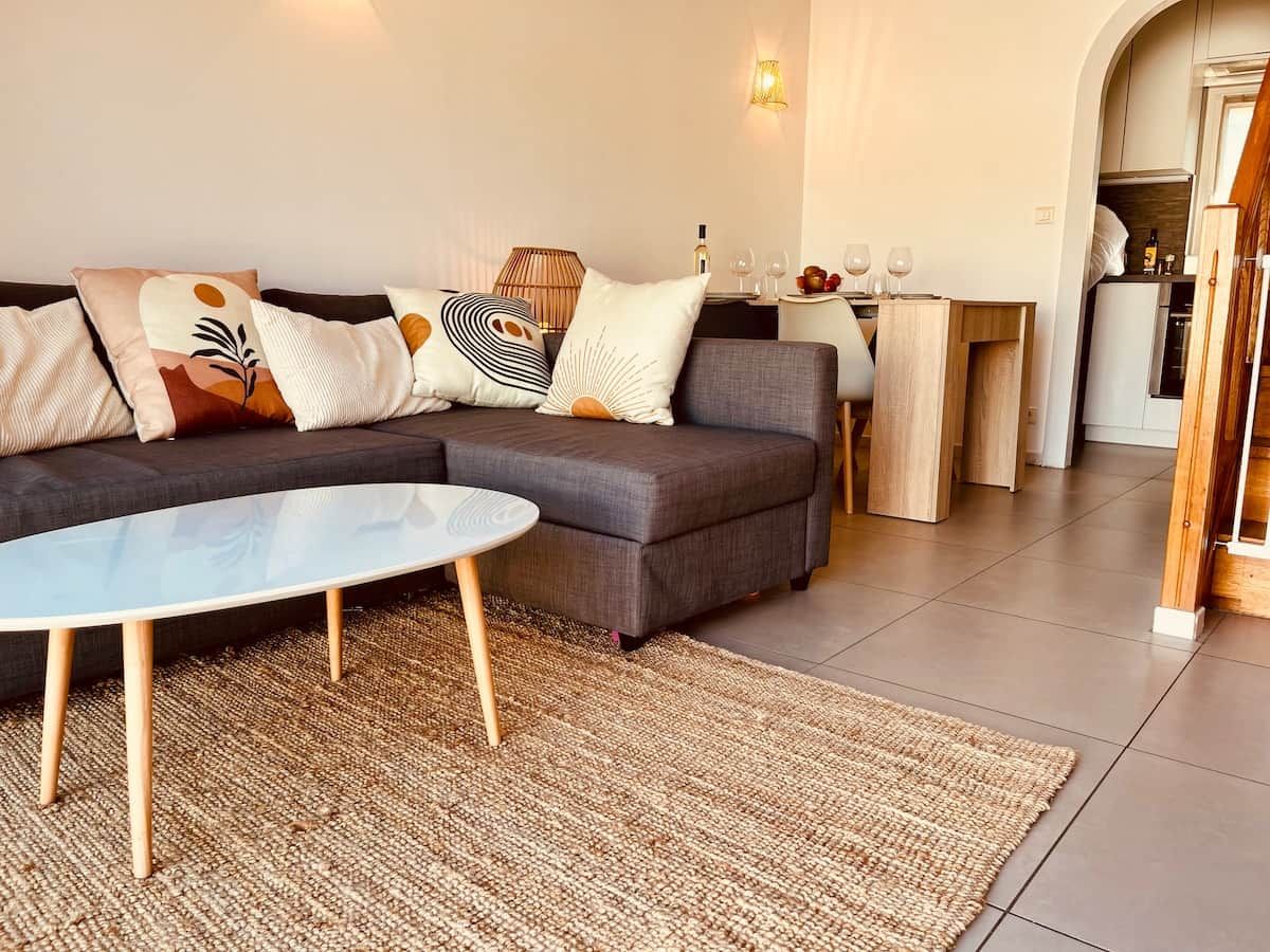 Una sala de estar moderna con un sofá modular, una mesa de centro redonda y una cocina visible a través de un arco.