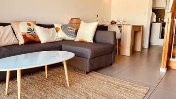 Una sala de estar moderna con un sofá modular, una mesa de centro redonda y una cocina visible a través de un arco.
