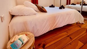 Ein Schlafzimmer mit einem Bett, einem Nachttisch mit Büchern, einem Spiegel und einem Fenster mit Vorhängen.