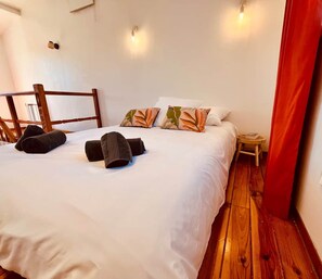 A neatly made bed with rolled towels, a small bedside table with a book, and a wooden floor. - Cozy Air-Conditioned Apartment – Simiane-Collongue (13) (Simiane-Collongue)