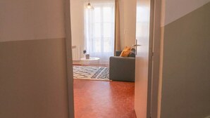 En hall med ett golv täckt av röda plattor, som leder in till ett vardagsrum med en soffa och en hängande lampa.