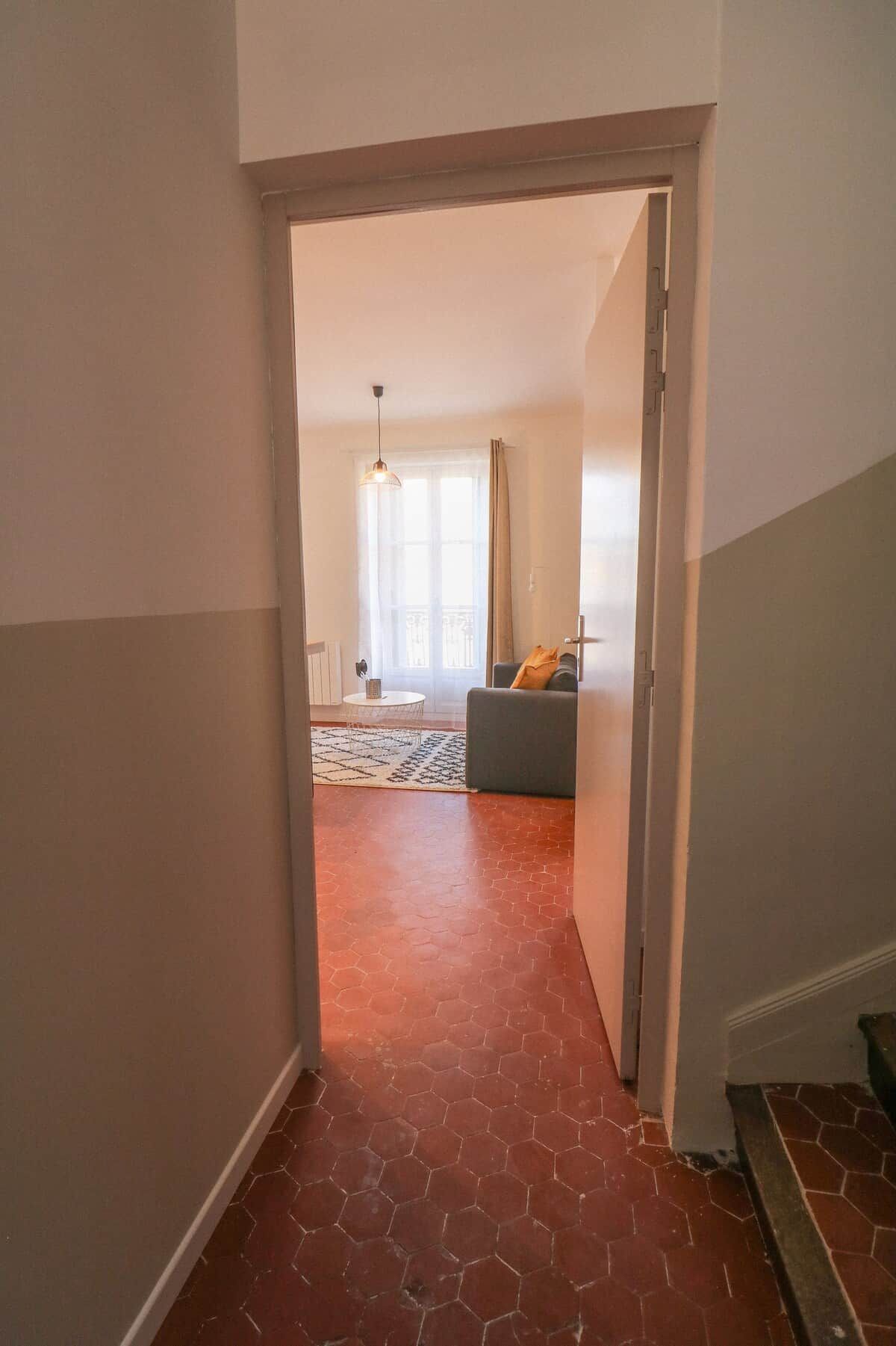 Um corredor com piso de azulejos vermelhos que leva a uma sala de estar com sofá e luminária pendente.