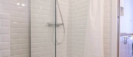 A glass-enclosed shower with a handheld showerhead and a wall-mounted faucet.