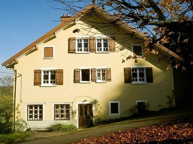 A two-story building with a symmetrical facade, multiple windows with shutters, and a central entrance.