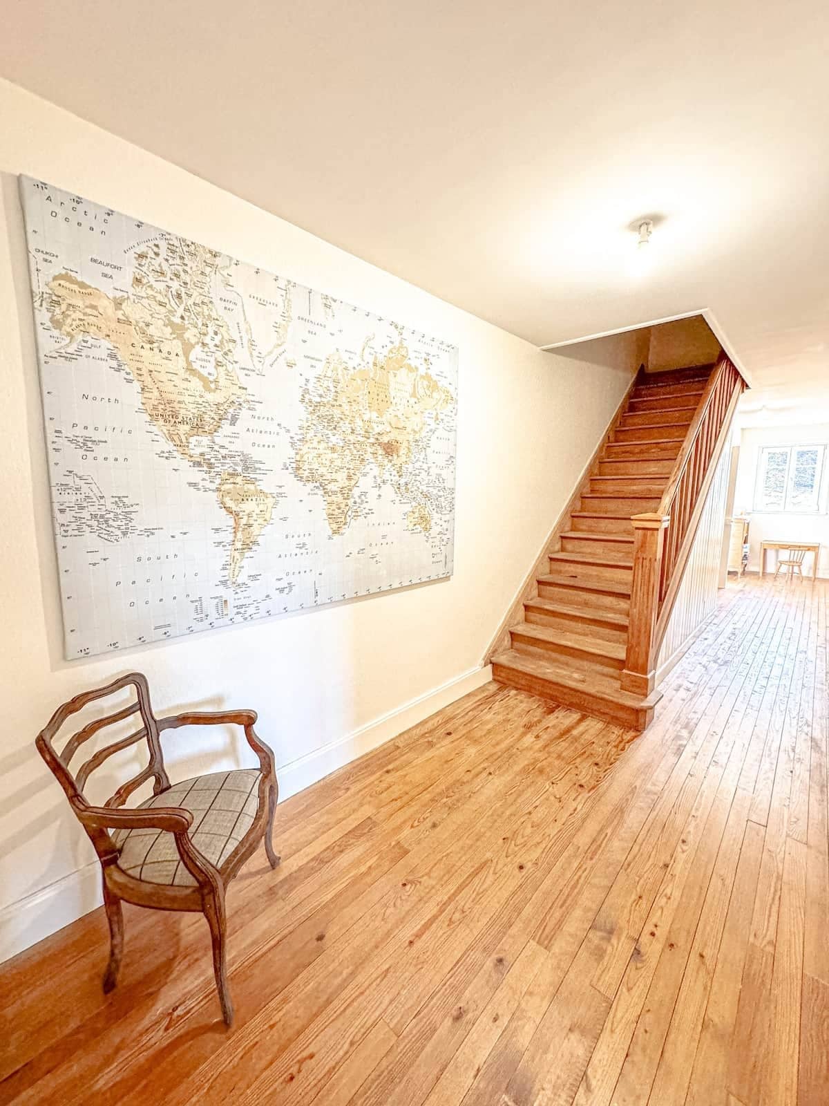 A spacious room with a large world map on the wall, a wooden staircase, and a wooden chair.