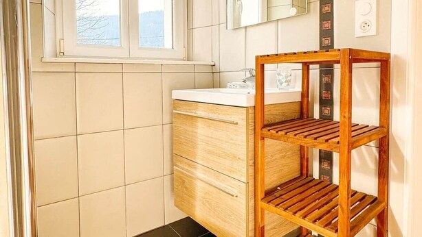 Ein Badezimmer mit einem Holzbadezimmerhocker, einem Spiegel und einem Regal.