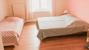 Ein Zimmer mit zwei Betten, einem Heizkörper, einem Fenster mit Vorhängen und einer Lampe.