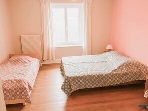 Ein Zimmer mit zwei Betten, einem Heizkörper, einem Fenster mit Vorhängen und einer Lampe.