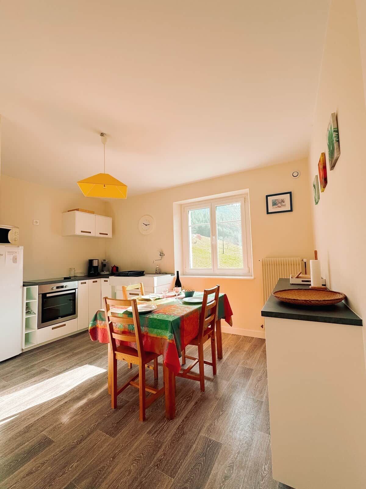 A kitchen with a dining table, chairs, a yellow pendant light, and a window with a view.