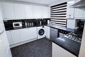 Una cocina compacta con armarios blancos, lavadora, lavavajillas, microondas y estufa.