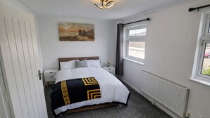 Ein Schlafzimmer mit Bett, Nachttisch, Fenster, Heizkörper und einem Bild an der Wand.