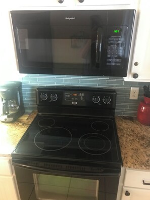 A kitchen with a black microwave, stove, and oven, a coffee maker, and a red water dispenser. - Beautiful 2-bedroom oceanfront condo sleeps up to 7 in St. Augustine Beach (St. Augustine)