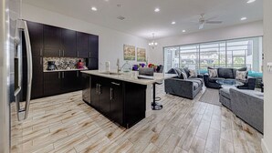 Una cocina moderna con armarios oscuros, una isla central y una zona de comedor con sofá y mesa de centro.