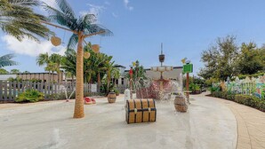 Un área con temática tropical, palmeras, una fuente de agua y un cofre del tesoro.