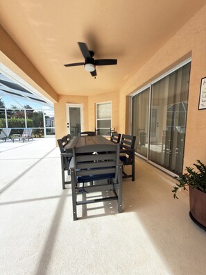 Une terrasse extérieure avec une table et des chaises, un ventilateur de plafond et une porte-fenêtre coulissante.