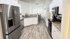 A modern kitchen with a stainless steel refrigerator, granite countertops, and a central island. - Quaint, modern 3-bedroom house in charming, historic Inverness Florida. (Inverness)