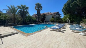 A swimming pool with lounge chairs and palm trees. - ÜNLÜ OTEL (Fethiye)