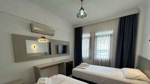 A hotel room with two beds, a desk, a TV, and an air conditioning unit. - ÜNLÜ OTEL (Fethiye)