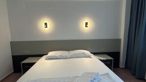 A hotel room with a large bed, two bedside tables, a nightstand, and a wall-mounted light fixture. - ÜNLÜ OTEL (Fethiye)