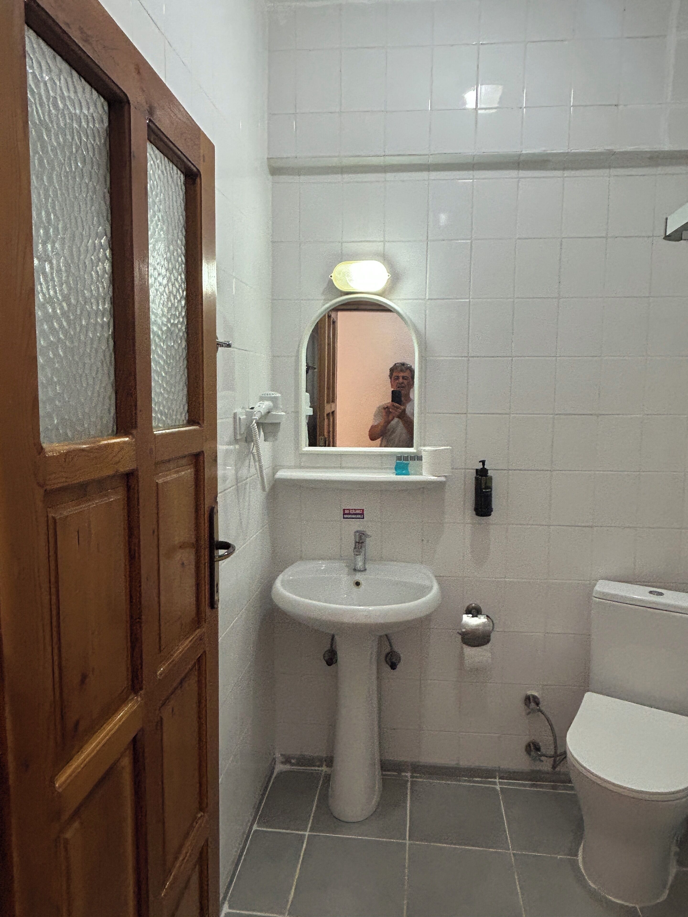 Un baño con puerta de madera, un lavabo blanco, un espejo, un inodoro y una zona de ducha.
