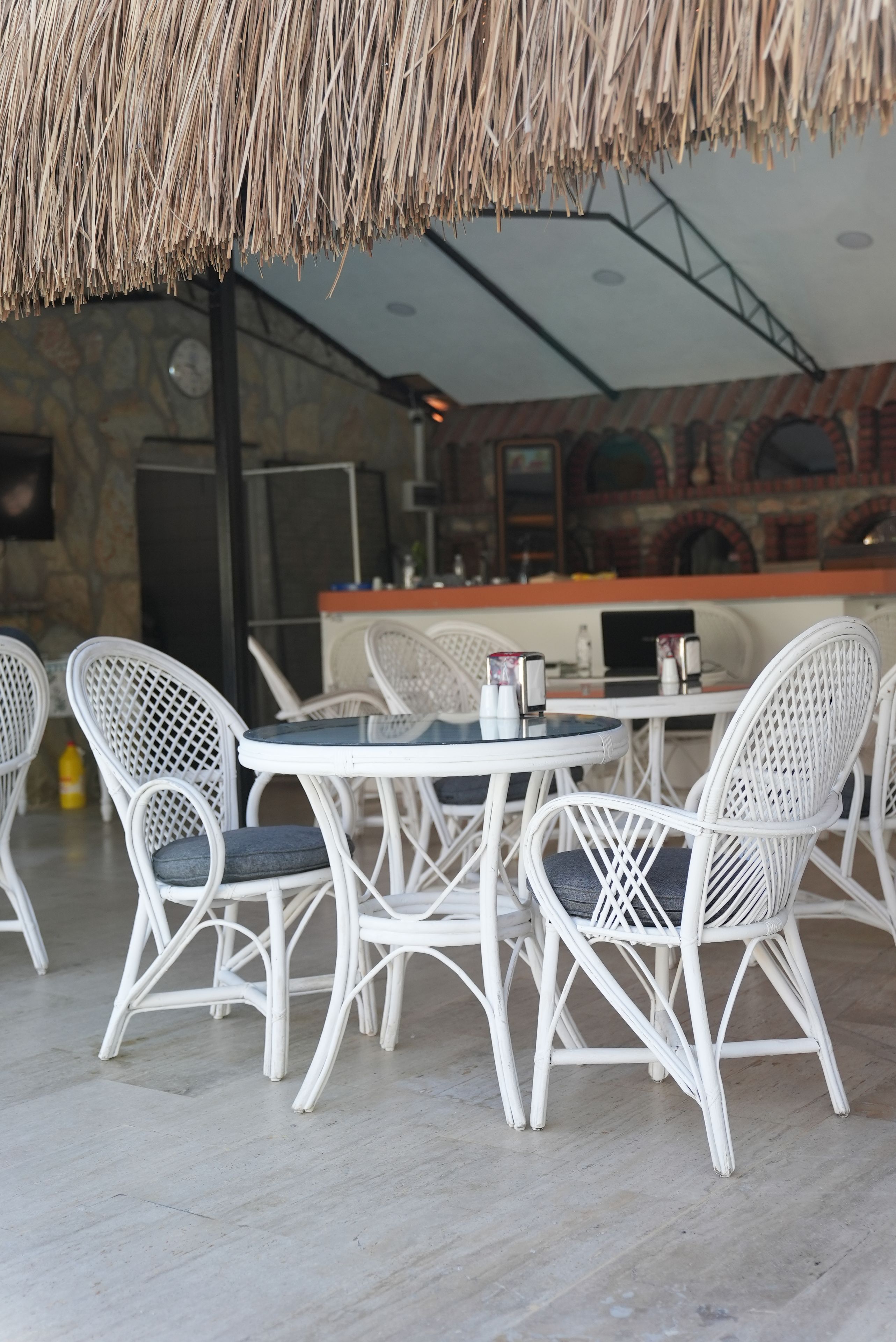 A restaurant with white wicker furniture, a round table, and a thatched roof.