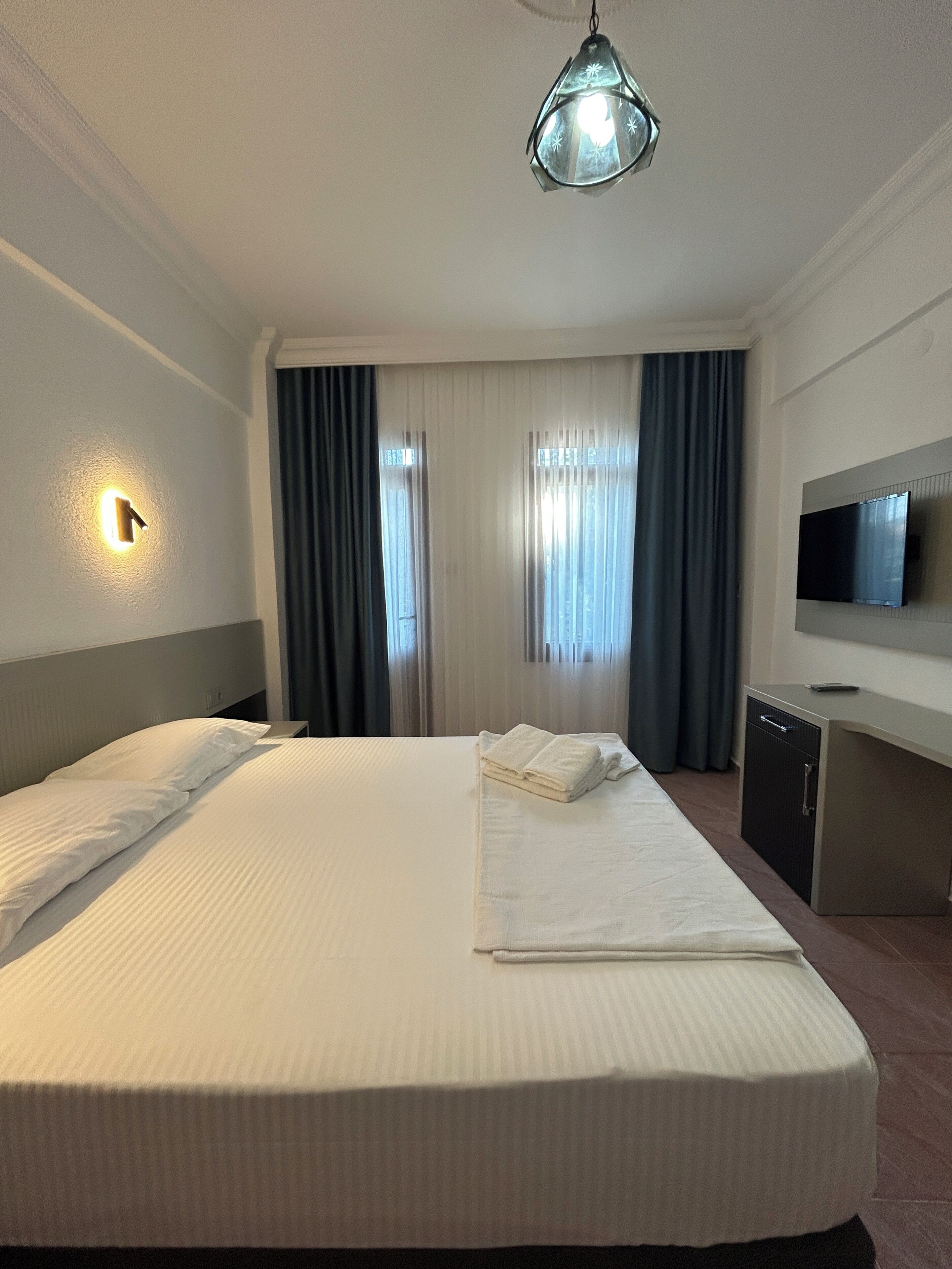 A hotel room with a bed, a flat-screen TV, a desk, and a ceiling light fixture.