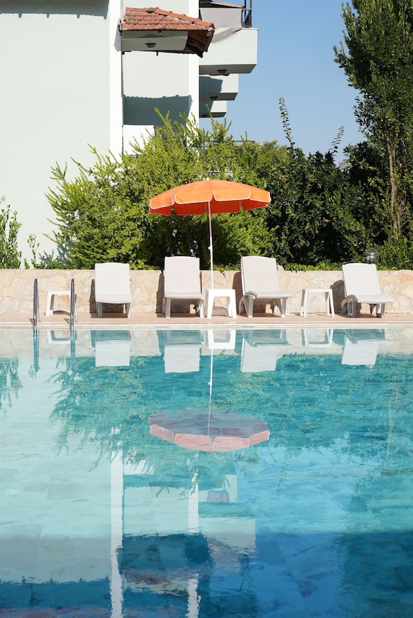 Una piscina con agua azul cristalina, rodeada de sillas de descanso blancas y un paraguas naranja.