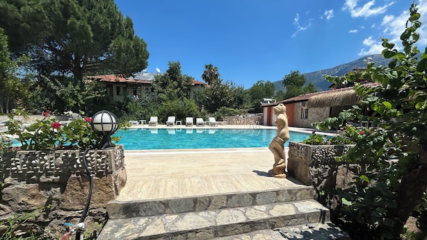 A stone staircase leading to a pool with lounge chairs and a statue. - ÜNLÜ OTEL (Fethiye)