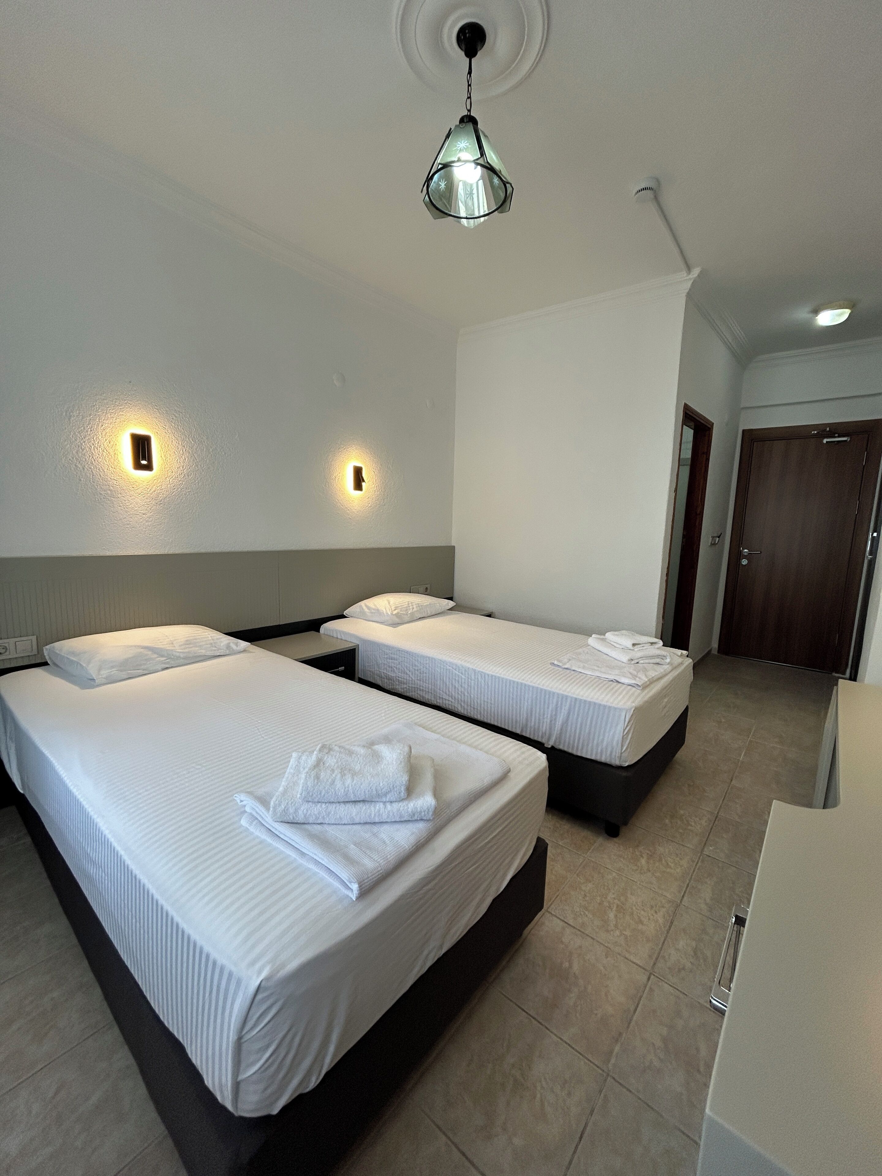 A hotel room with two beds, a ceiling light fixture, and a door.