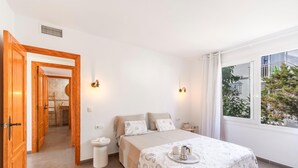 Een slaapkamer met een bed, nachtkastje en een raam met uitzicht op groen.