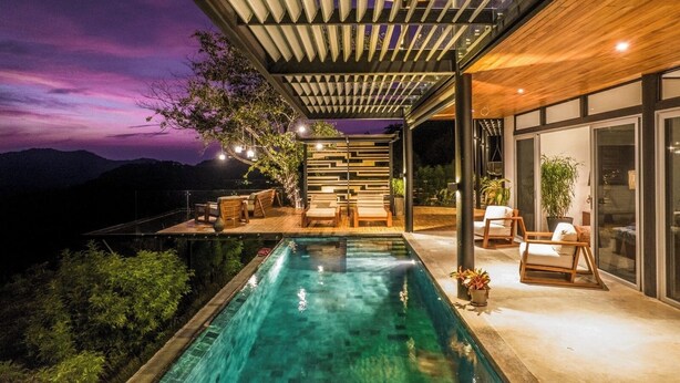 A modern outdoor pool area with a wooden deck, lounge chairs, and a view of the mountains at dusk. - Ocean view · infinity pool · fully equipped private spa (Playa Grande)