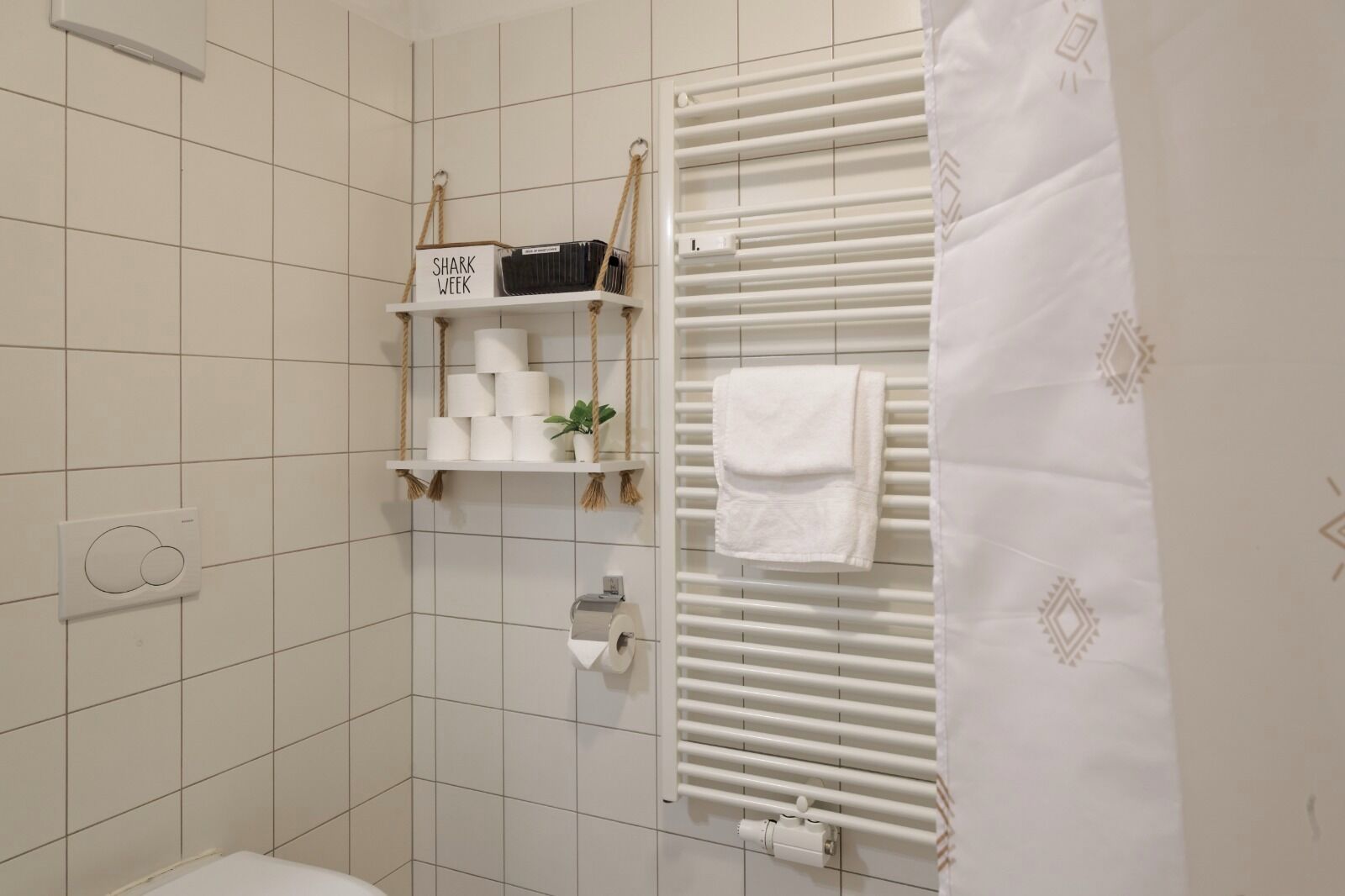 A bathroom with a toilet, a towel rack, a shelf with toiletries, and a radiator.