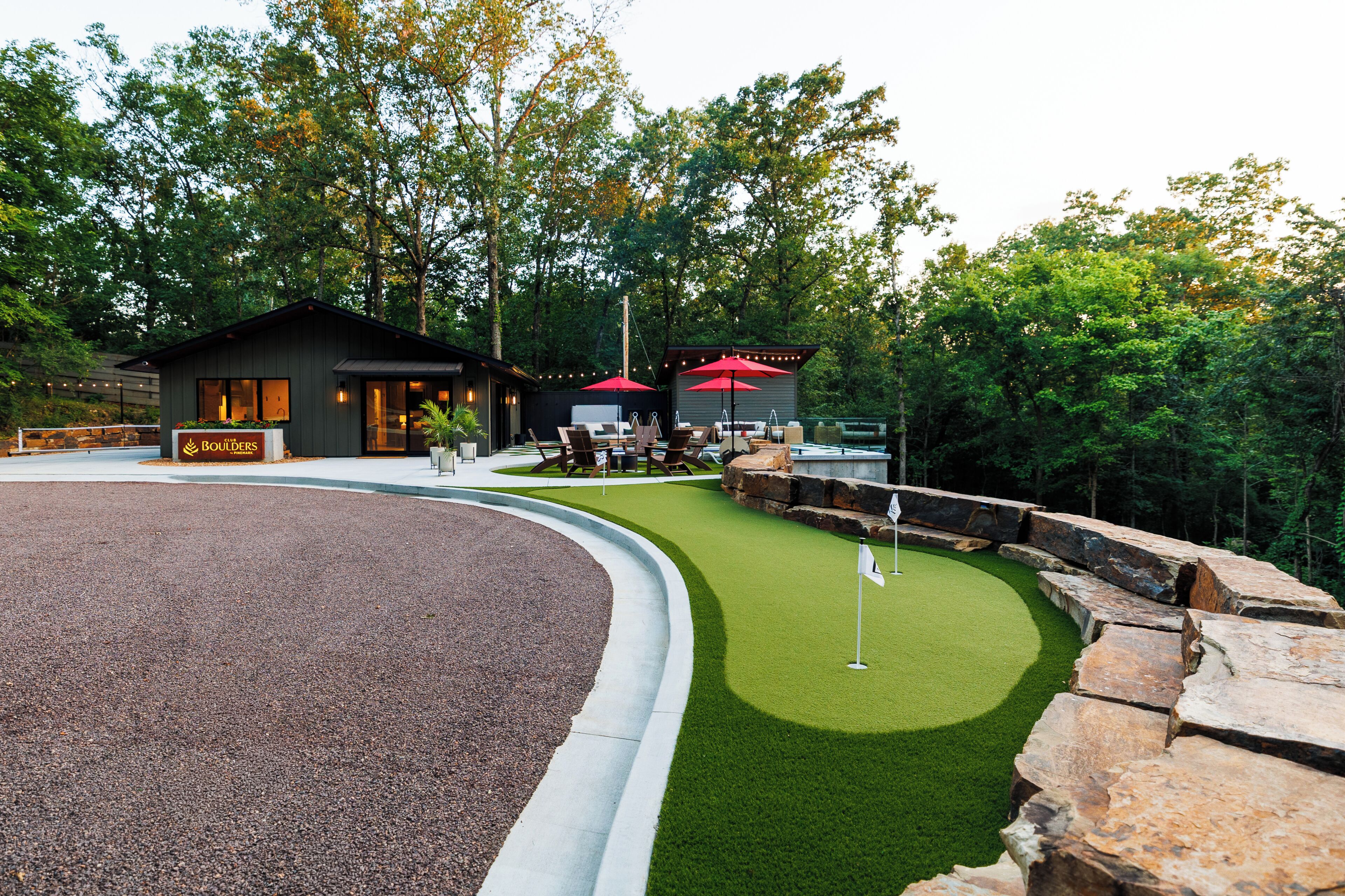 A golf course with a clubhouse, a putting green, and a seating area with umbrellas.