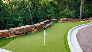 Un parcours de golf doté d’un green d’entraînement, entouré d’un mur de pierre et d’une végétation dense.