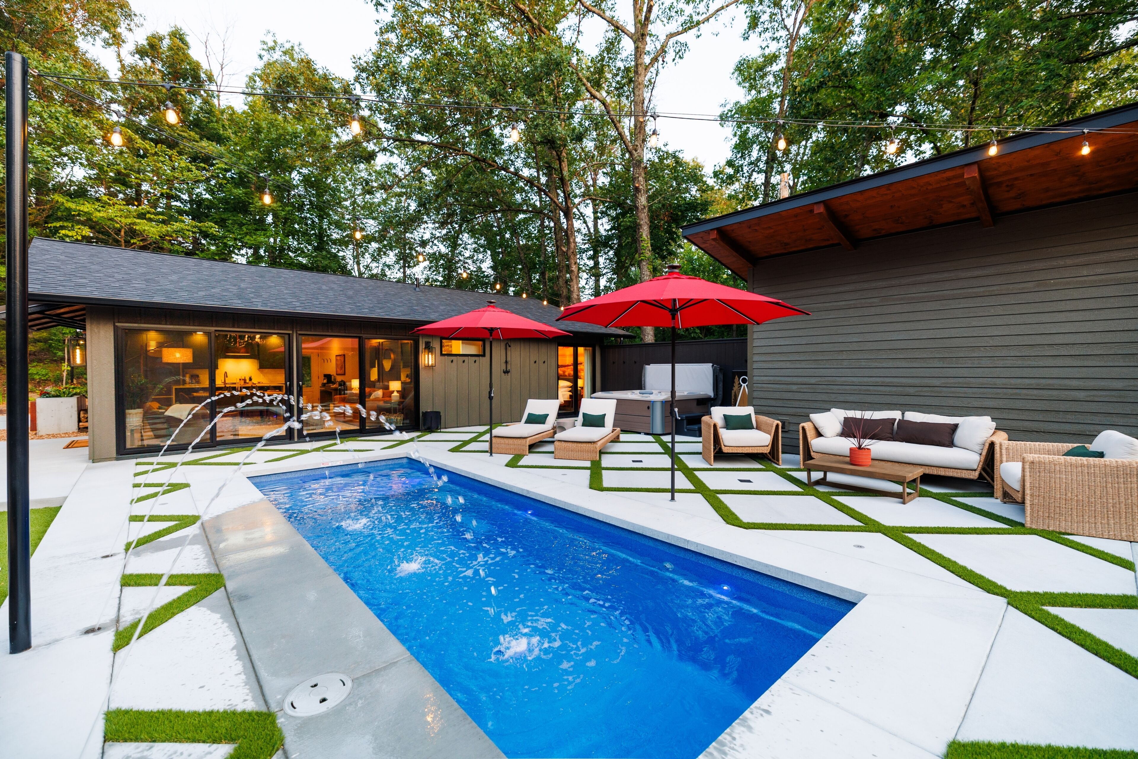 A modern outdoor pool area with lounge chairs and umbrellas, surrounded by a wooden deck and a glass-enclosed building.