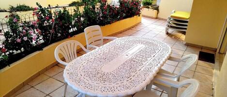 A patio with a white table and chairs, surrounded by yellow walls and a flower bed.
