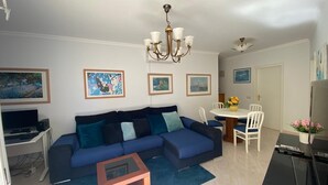 A living room with a sofa, a coffee table, a dining table with chairs, and a chandelier. - Ground-floor apartment with spacious terraces, 15 minutes from the marina and Falésia Beach (Quarteira)