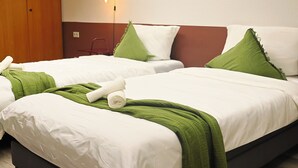Une chambre d’hôtel avec deux lits, chacun agrémenté de draps blancs et de touches de vert, une armoire en bois et un luminaire fixé au mur.