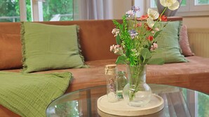 Une table en verre sur laquelle se trouvent un vase de fleurs, un bocal en verre et une petite bouteille, le tout posé sur une table ronde en verre.