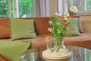 A glass table with a vase of flowers, a glass jar, and a small bottle on a round glass table.