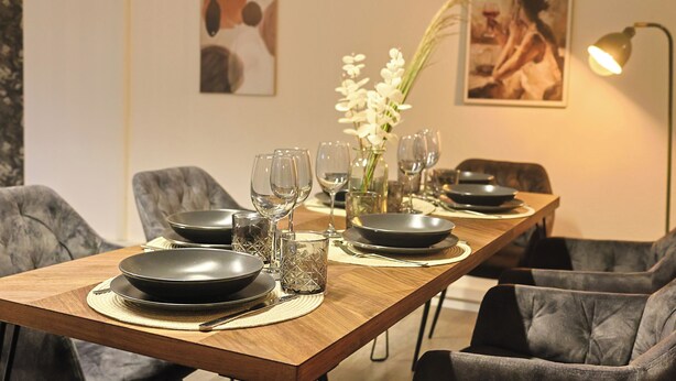 Une table à manger dressée avec des assiettes, des verres et un vase de fleurs, entourée de chaises et agrémentée d’œuvres d’art accrochées aux murs.