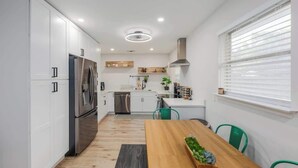 Une cuisine moderne avec des meubles blancs, des appareils électroménagers en acier inoxydable et une table à manger en bois.
